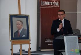 Po lewej stronie na sztaludze obraz przedstawiający wizerunek Seweryna Pieniężnego, po prawej przy mównicy z mikrofonem stoi Piotr Grzymowicz, prezydent Olsztyna