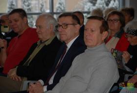 Na pierwszym planie PIotr Grzymowicz, prezydent Olsztyna oraz szef Nowego Życia Olsztyna, Leszek lik, siedzą wśród uczestników uroczystości. W tle pozostali uczestnicy.