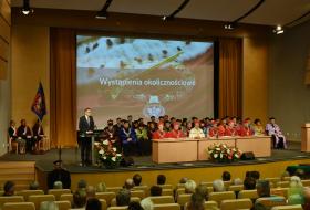 na zdjęciu widoczni siedzący członkowie senatu UWM, przy mónicy przemawia prezydent Olsztyna, w tle widoczny ekran prezentacyjny oraz poczet sztandarowy uczelni