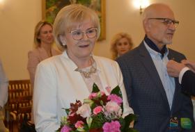 Na pierwszym planie para jubilatów 50-lecia pożycia małżeńskiego. Jubilatka trzyma bukiet kwiatów. W te dwie uczestniczki uroczystości.
