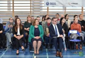 Na pierwszym planie prezydent Olsztyna Piotr Grzymowicz siedzi w pierwszym rzędzie podczas uroczystości ślubowania piewrszakó z SP.30. W tle siedzą uczestnicy spotkania - kadra pedagogiczna oraz rodzice. 
