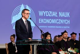 Piotr Grzymowicz stoi przy mikrofonie podczas inauguracji roku akademickiego na wydz. nauk ekonomicznych UWM