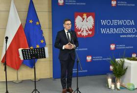 Zdjęcie przedstawia pzremawiającego prezydenta Olsztyna stąjącego na tele flagi polski i unii europejskiej