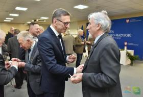 Zdjęcie przedstawia mężczyzne oraz prezydenta Olsztyna którzy ściskają sobie dłoń oraz dzielą się opłatkiem 